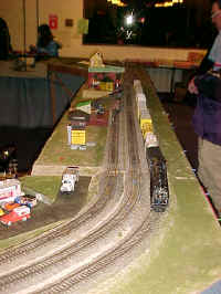 A 4-8-4 Northern locomotive is on the point of a freight passing the accessory side of the RASG modular layout.